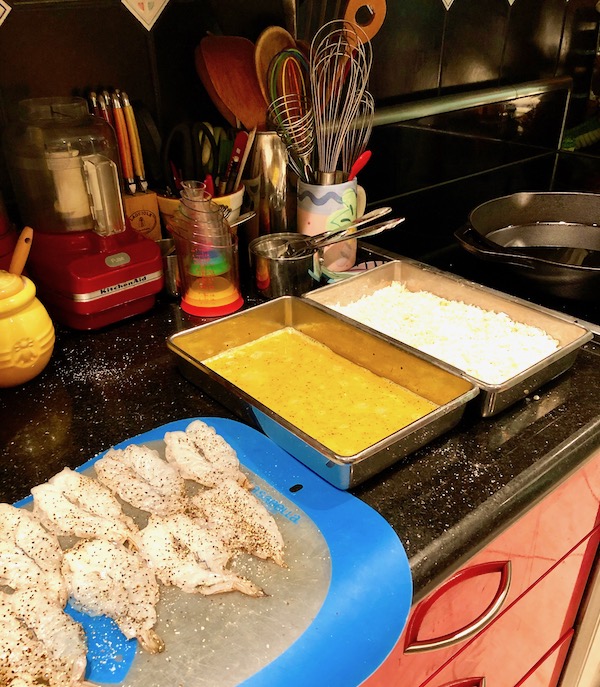 Seasoned butterflied shrimp on a blue edged plastic cutting board, and two pans one with egg and one with panko/coconut mixture for my Coconut Shrimp with Strawberry Mango Salsa