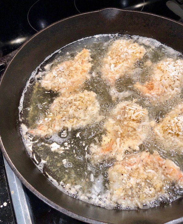 A cast iron pan filled with oil and coconut crusted shrimp cooking on first side for my Coconut Shrimp with Strawberry Mango Salsa