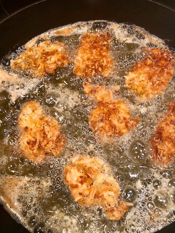 A cast iron pan filled with oil and golden brown coconut coated shrimp for my Coconut Shrimp with Strawberry Mango Salsa