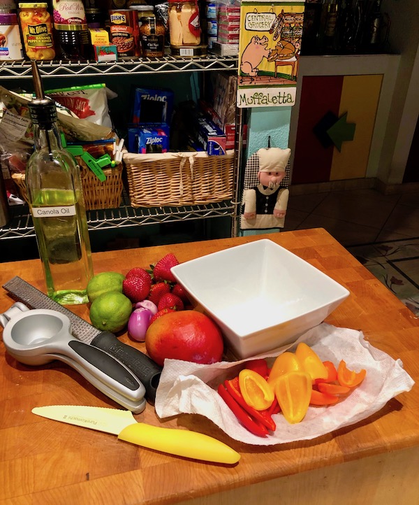 A butcher block topped with yellow knife, citrus juicer, assorted fruit and a white bowl for my Coconut Shrimp with Strawberry Mango Salsa