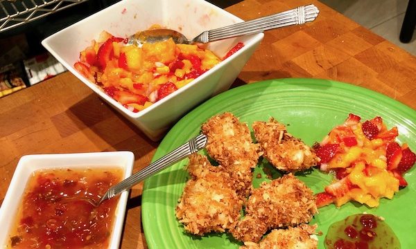 A butcher block topped with a lime green plate that holds golden brown coconut shrimp, salsa and sauce plus white square bowls of the salsa and sauce for my Coconut Shrimp with Strawberry Mango Salsa