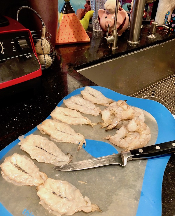 A blue edged plastic cutting board topped with a knife and shrimp for Coconut Shrimp with Strawberry Mango Salsa