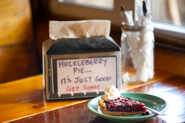 A napkin holder with the words huckleberry pie on it and a green plate with a slice of pie from Discover a Taste of Montana
