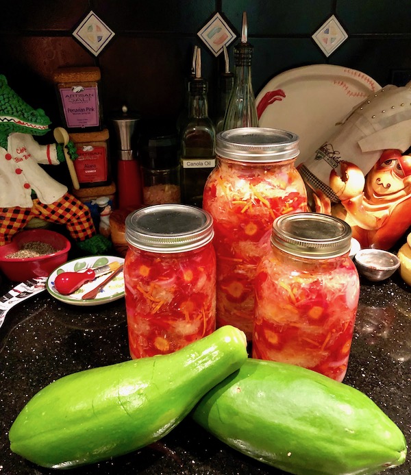 One large and two smaller mason jars of Green Papaya Salad with two papayas on a kitchen counter.