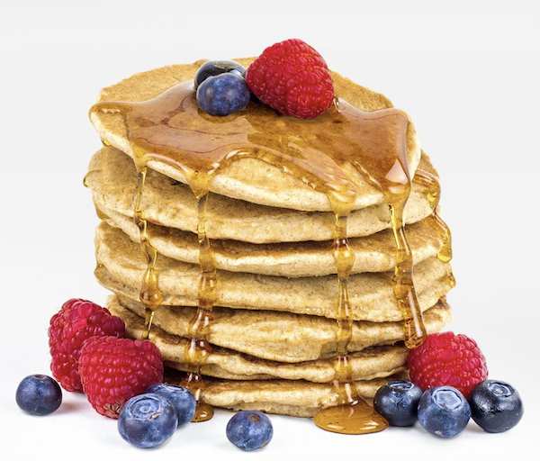 A tall stack of Keto Pancakes dripping with syrup and berries.