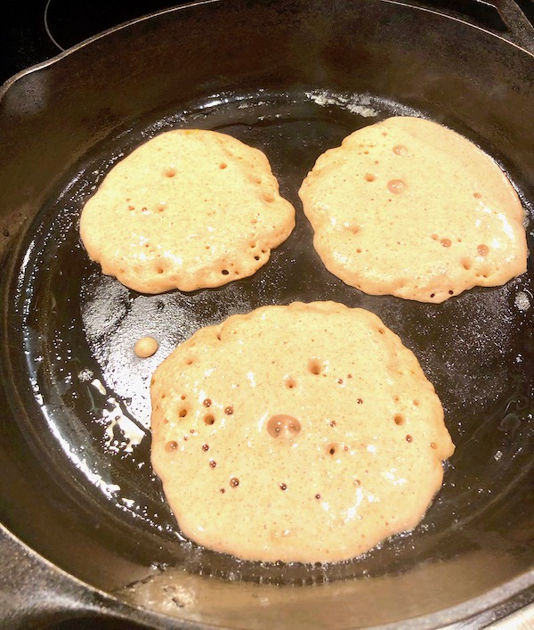 A cast iron skillet with 3 Keto Pancakes cooked on one side and ready to be flipped