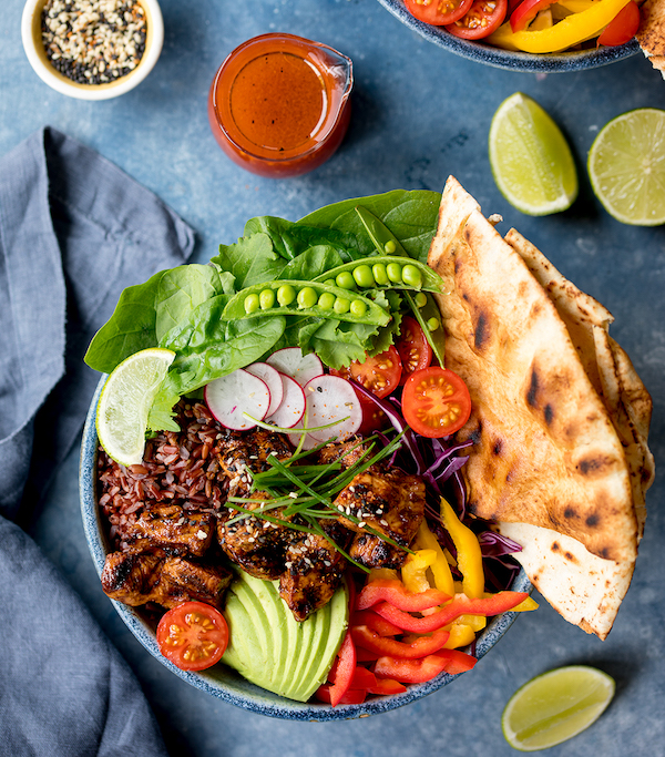 A black bowl filled with pea pods, chicken, vegetables and pita bread from Seriously Good Salads