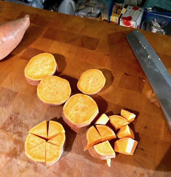 Slices and wedges of sweet potato on a butcher block for Cinnamon Garlic Roasted Sweet Potatoes