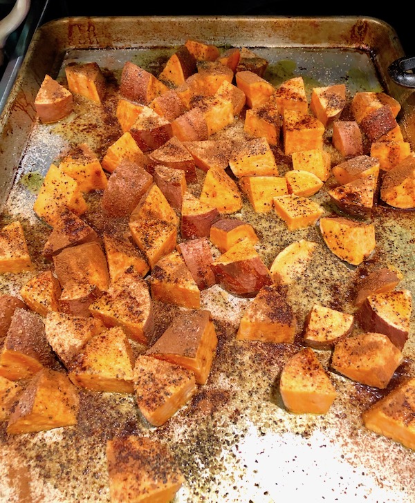 Seasoned sweet potato wedges on a sheet pan for Cinnamon Garlic Roasted Sweet Potatoes