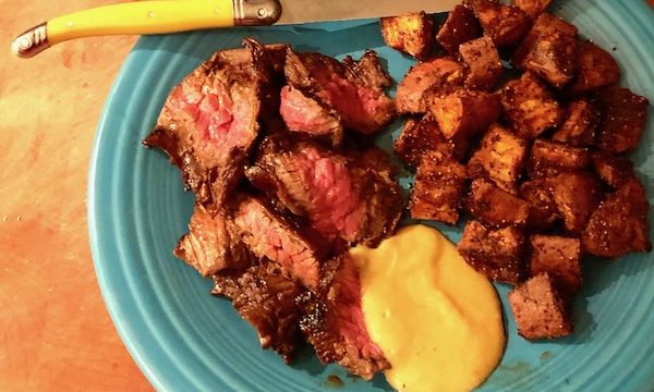A turquoise plate topped with sliced steak, mustard sauce and Cinnamon Garlic Roasted Sweet Potatoes