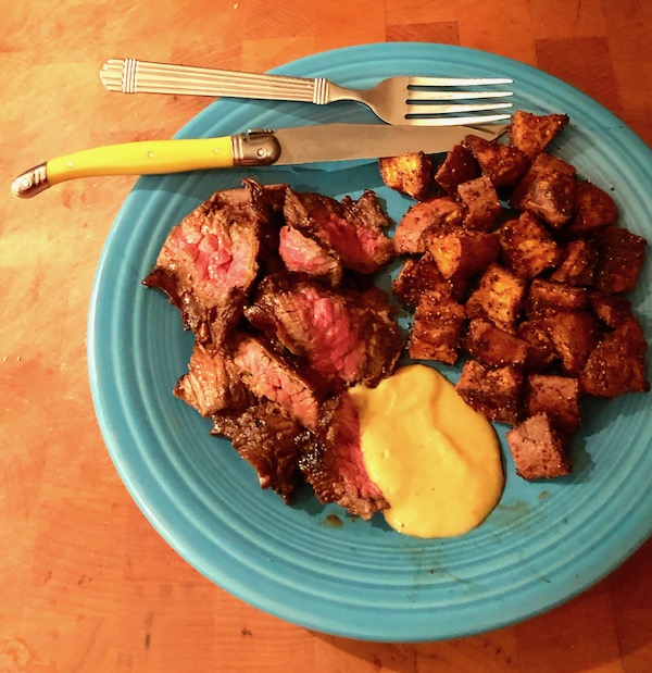 A turquoise plate topped with sliced steak, mustard sauce and Cinnamon Garlic Roasted Sweet Potatoes