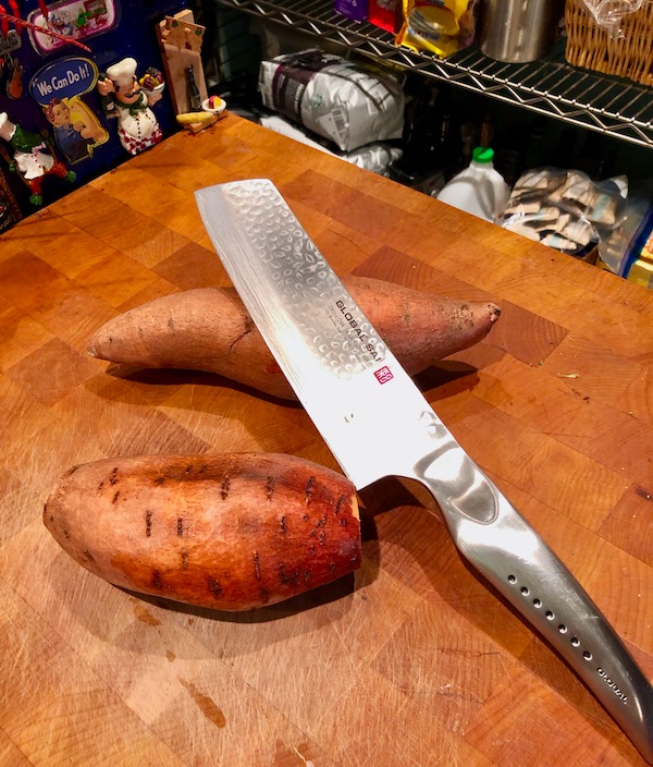 Two sweet potatoes and a knife on a butcher block for Cinnamon Garlic Roasted Sweet Potatoes