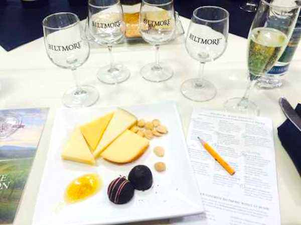 A white clothed table topped with cheeses and glasses of wine, a pencil; and paper from Fall Adventures In Asheville, NC