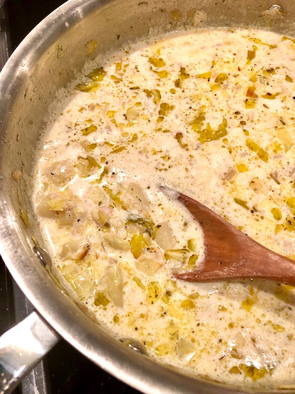 A pan of New England Clam Chowder being stirred with a wooden spoon.