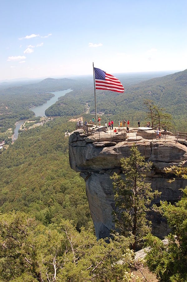A big chimney shaped rock in a park with the American flag at the tip from Fall Adventures In Asheville NC