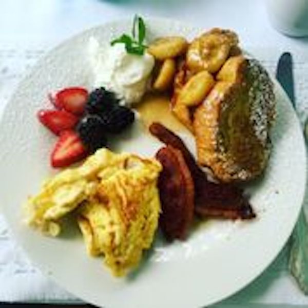 A white plate loaded with scrambled eggs, French toast, bacon, fruit and whipped butter from Beyond The Bayou