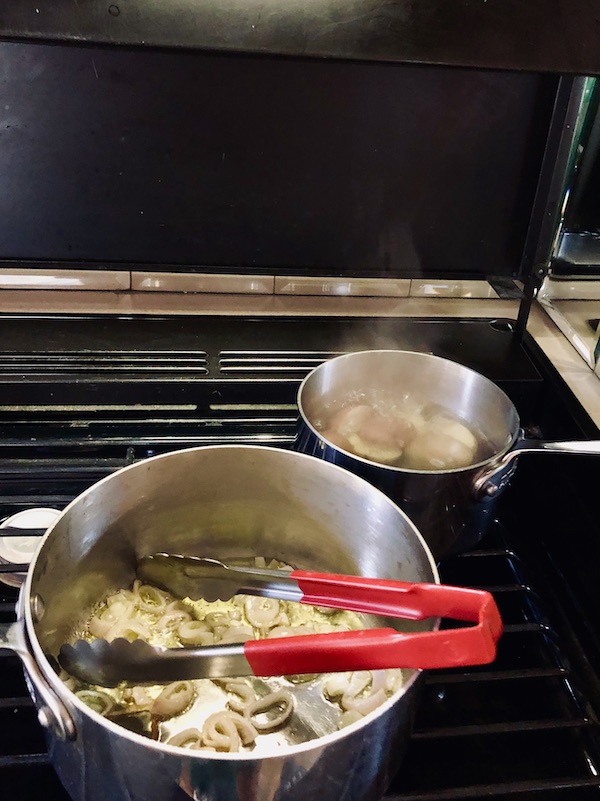 Pots on a gas stove with red handled tongs