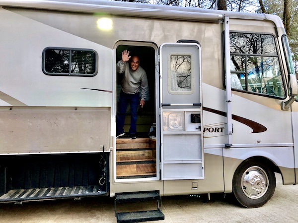 A man in a grey sweatshirt waving at the open door of an RV at the 1st Stop - Greensboro, Georgia