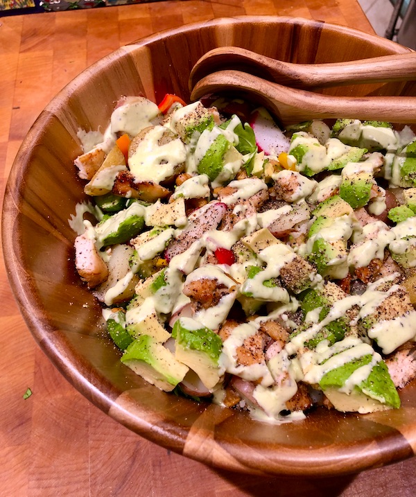 A teak salad bowl filled with a colorful salad drizzled with creamy white dressing