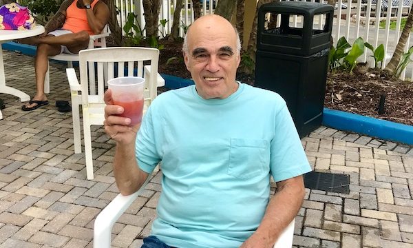 A man in an aqua T-shirt enjoying a cocktail poolside at Tropical Palms RV Resort