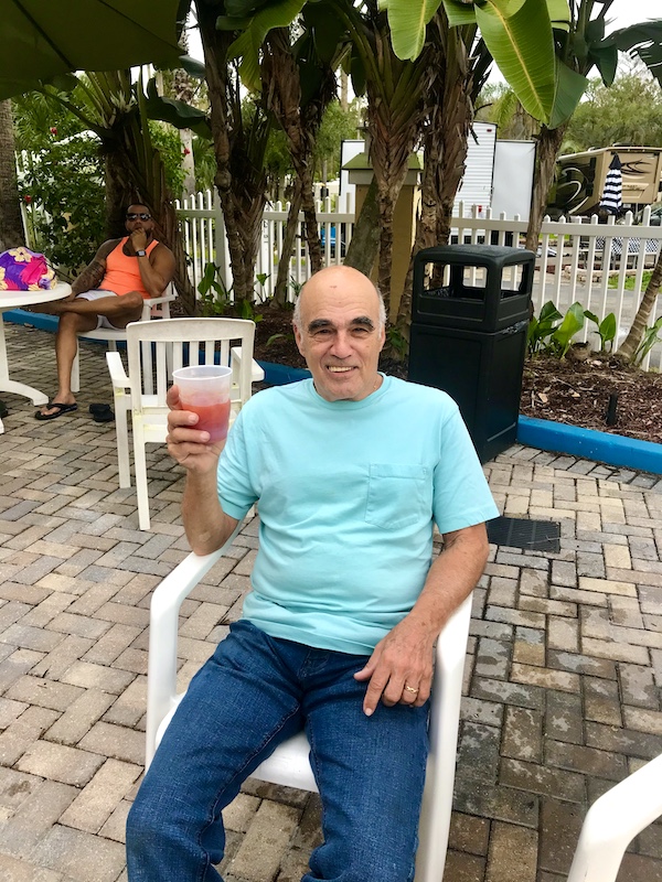 A man in an aqua T-shirt enjoying a cocktail poolside at Tropical Palms RV Resort