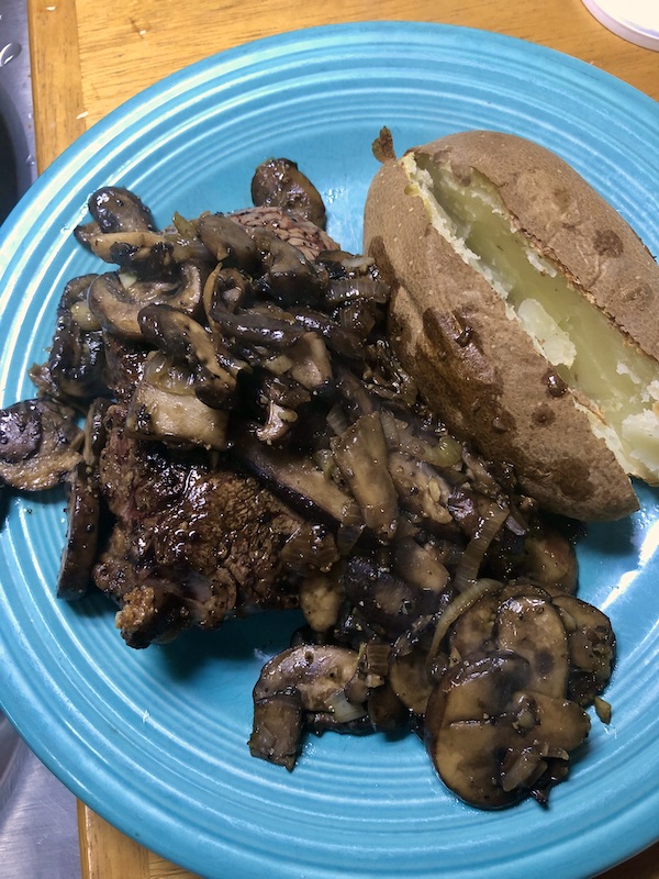 Steak topped with mushroom with a baked potato alongside on a blue plate.