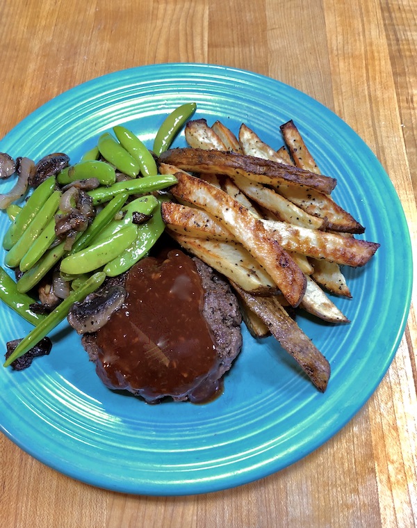 A turquoise plate topped with a sauced burger, sugar snap peas and mushrooms and French Fries.