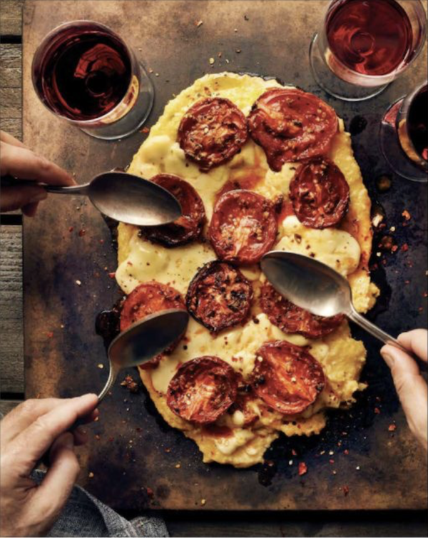 Hands with spoons digging in to polenta topped with roasted tomatoes and cheese from Wine Country Table