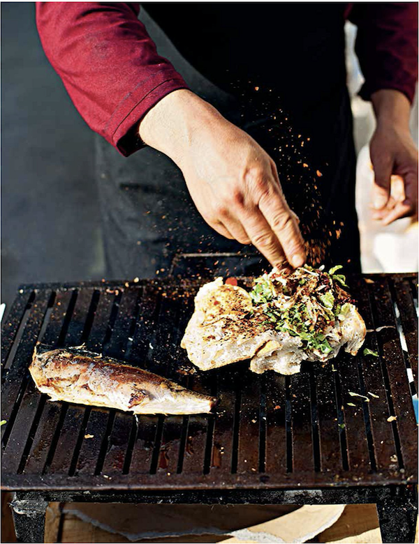A person seasoning food on a grill from Istanbul Cult Recipes