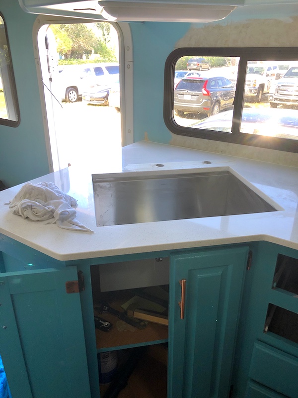 An RV kitchen with white quartz counter and deep single bowl stainless steel sink from Our RV Renovations Update