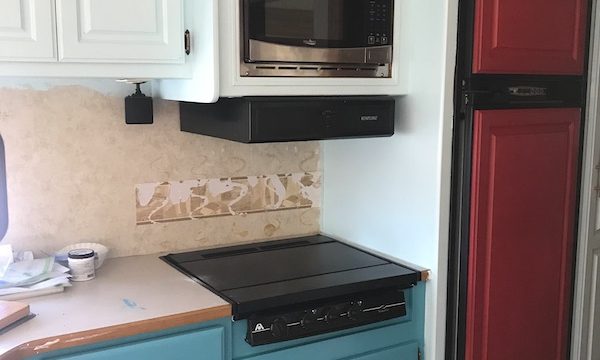 An RV kitchen with light aqua upper cabinets, teal base cabinets and red refrigerator doors from Our RV Renovations Update