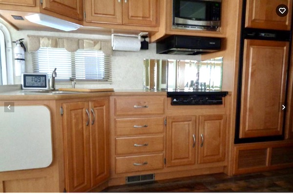 An RV kitchen with wood cabinetry and a mirror backsplash is before Our RV Renovations Update