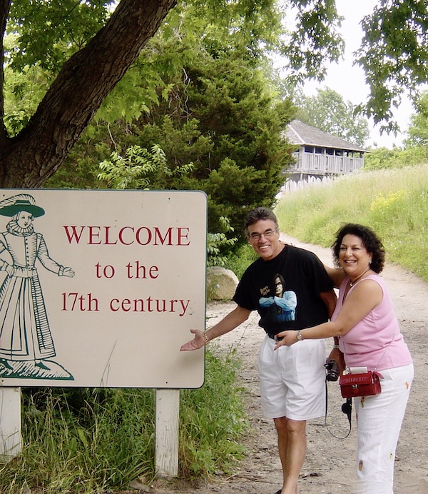 A couple pointing to a welcome sign from Plymouth Massachusetts