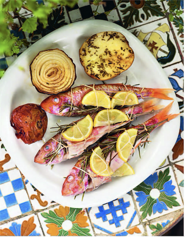 A white plate with assorted vegetables and 3 red fish topped with lemon slices from Barcelona Cult Recipes