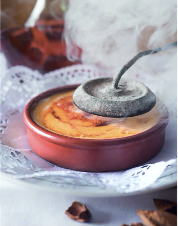 A creme brulee in a red dish being torched from Barcelona Cult Recipes