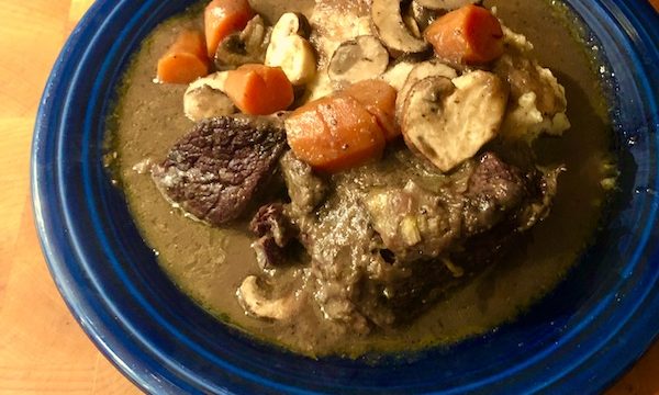 A dark blue bowl filled with Red Wine Braised Beef and mashed potatoes on a wood surface