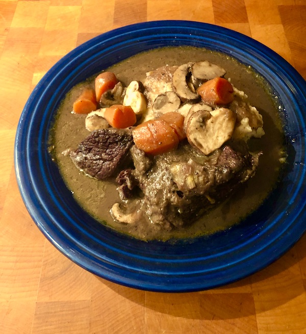 A dark blue bowl filled with Red Wine Braised Beef and mashed potatoes on a wood surface