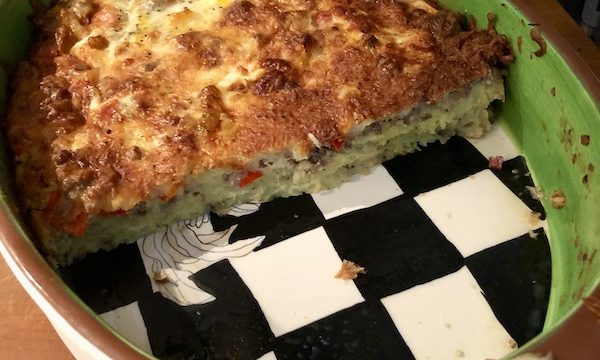 A potato and sausage casserole in an oval baking dish with black and white checked bottom from Easy Breakfast for Dinner Casserole