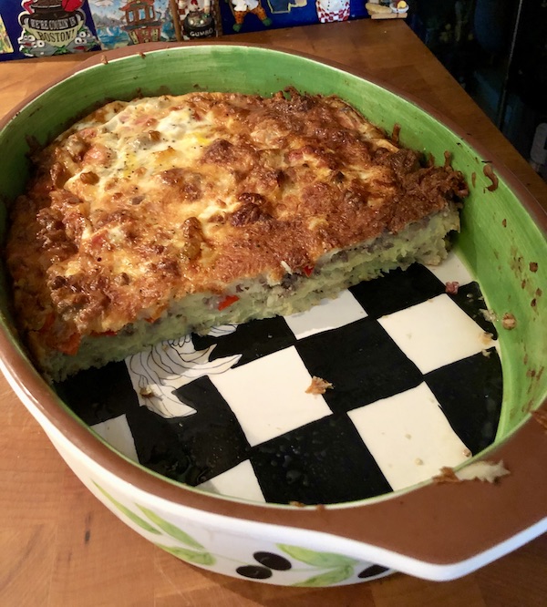 A potato and sausage casserole in an oval baking dish with black and white checked bottom from Easy Breakfast for Dinner Casserole