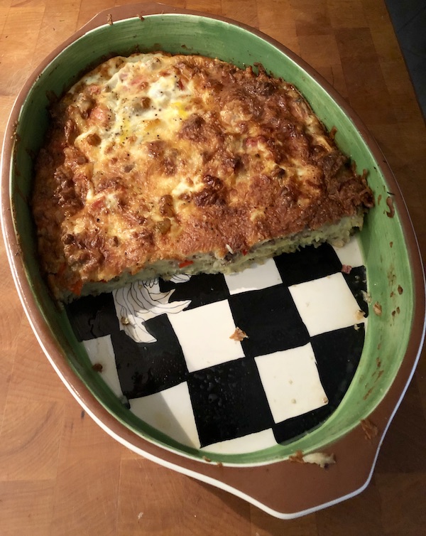 A potato and sausage casserole in an oval baking dish with black and white checked bottom from Easy Breakfast for Dinner Casserole