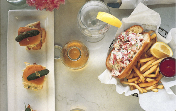 A basket lined with deli paper holding a lobster roll, fries, lemon wedge and ketchup from Los Angeles Cult Recipes