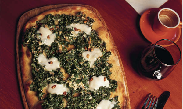 A whole rectangular pizza topped with cheese and kale on a wood table from Los Angeles Cult Recipes