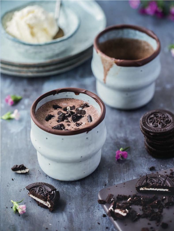 A pair of ceramic mugs filled with cookies and cream milkshakes with oreo cookies from New York Capital of Food