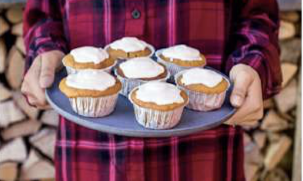 A woman in red and black plaid holding a tray of iced muffins from Taste the Wild