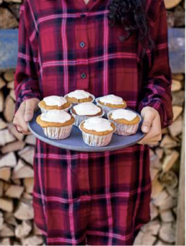 A woman in red and black plaid holding a tray of iced muffins from Taste the Wild