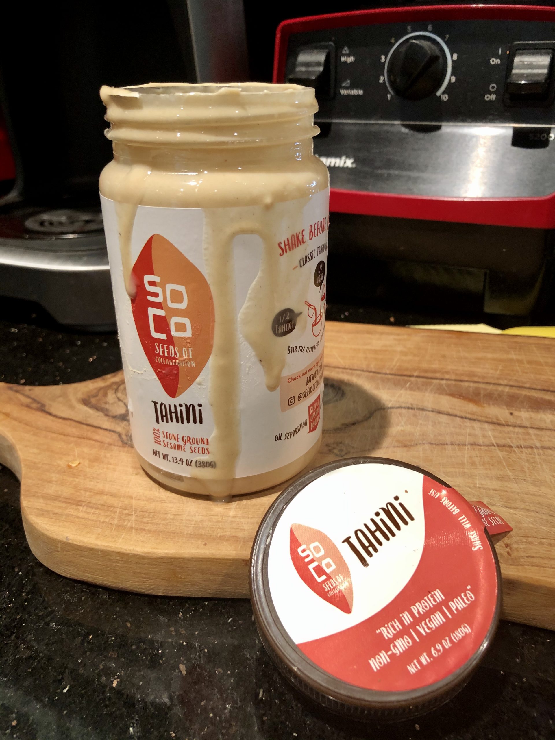 An open jar of tahini siting on a wood board for Salted Chocolate Covered Halvah