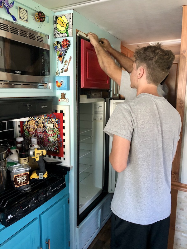 Two men removing a fridge with red doors from Living Our Dream