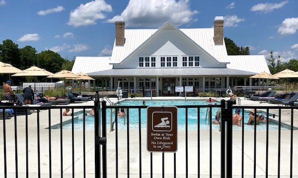 Black fence and gate leading to a pool and large gray building with white roof at CreekFire RV Resort Savannah