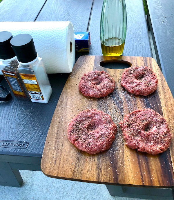 Four uncooked burgers on a cutting board with salt and pepper mills, paper towel roll and olive oil from Grillin' and Chillin' in North Myrtle Beach