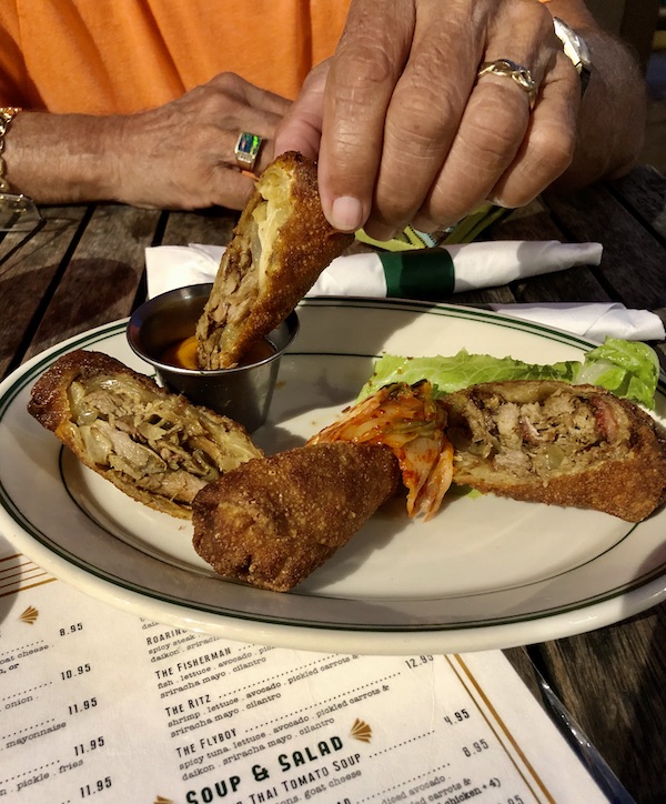A plate with egg rolls and a man's hand dipping a piece of egg roll into sauce from Little Duck Diner, Savannah